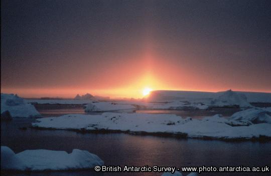 Sunset with Sun pillar across icebergs. The sun pillar is created by ice crystals in the air reflecting sunlight.