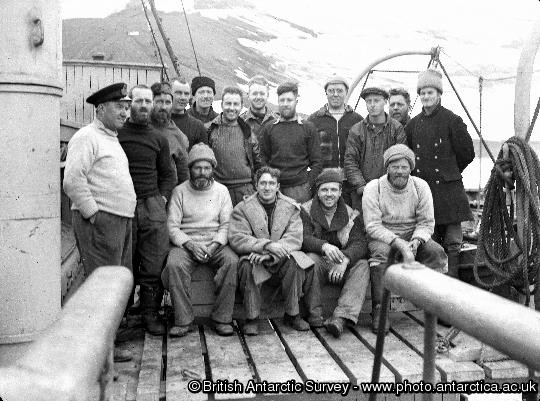 Operation Tabarin members on the deck of the Royal Navy ship H.M. S. Eagle at Deception Is.  Shows: (standing left to right) Berry, James, Matheson, Russell, Lamb, Farrington, Donnachie, Reece, Taylor, Davies, Smith, Back; (sitting left to right) Ashton, Blyth, Marshall, Flett.
