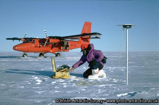 A glaciologist uses Twin Otter aircraft and GPS to survey the flow of the ice sheet.  The pole on which the antenna is mounted will be re-visited.  Measuring the speed of ice-flow allows glaciologists calculate whether the ice sheet is changing.  Here a glaciologist uses a Global Positioning System receiver to measure the position of an alumimium pole planted in the snow.  Remeasurement of its position after a year's movement will allow the ice-flow speed to be determined.  The measurement only takes one hour, so it can be efficiently supported by aircraft.