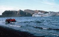 Tourists being taken ashore in an inflatable named Charles Darwin from tourist ship Hanseatic at Whalers bay, Deception Island , Cathedral Crags in background .